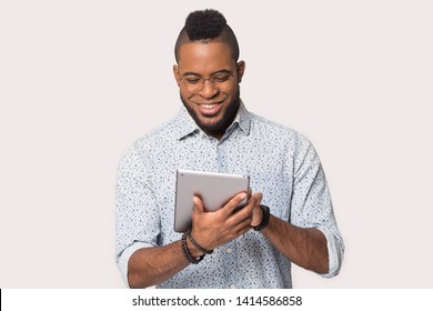 Smiling Mixed Race Man Isolated On Grey Or White Studio Background, Guy Holds Device Use Tablet Read Media News, Chatting With Friends, Modern Wireless Tech, Communication Online And E-dating Concept