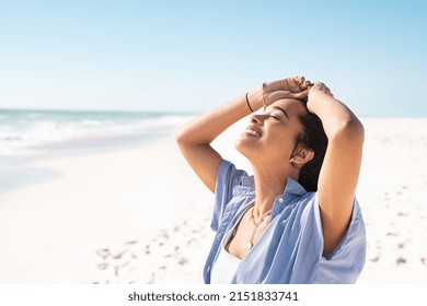 Smiling mixed race woman with eyes closed relaxing on beach. Beautiful young latin woman relaxing at seashore during summer. Happy carefree girl standing on the beach with white sand and copy space. - Shutterstock ID 2151833741