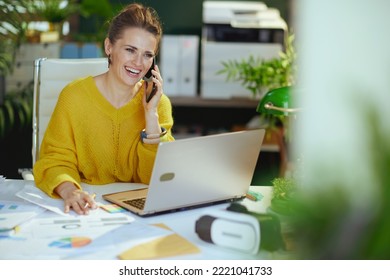 smiling modern 40 years old small business owner woman in yellow sweater with laptop speaking on a smartphone and working with documents in the modern green office. - Powered by Shutterstock