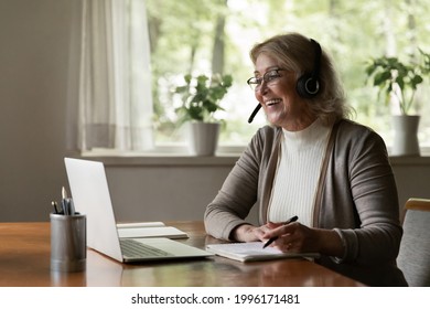 Smiling modern Caucasian old woman wear headset have fun use computer study online on gadget. Happy smart middle-aged female in earphones write note take distant course or training on laptop.