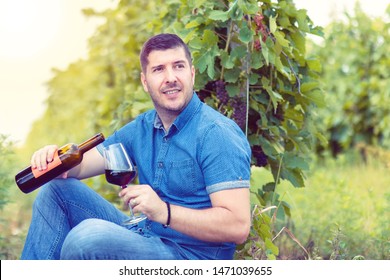Smiling Modern Man Pouring A Glass Of Red Wine While Relaxing In Vineyard – Happy Caucasian Male Enjoying Harvest Time Drinking Wine At Farm House Winery Countryside Looking For Friends