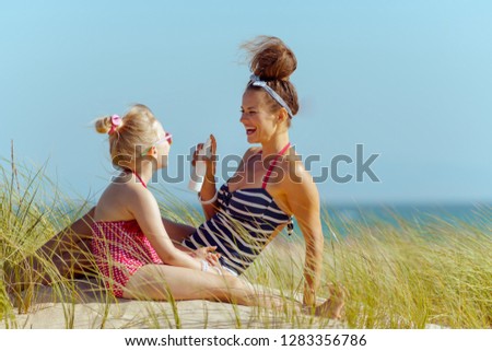 smiling modern mother and child in swimsuit on the ocean coast applying sun screen. sunscreen SPF or bug repellent or insect bite remedy or hair protection leave-in SPF conditioner.
