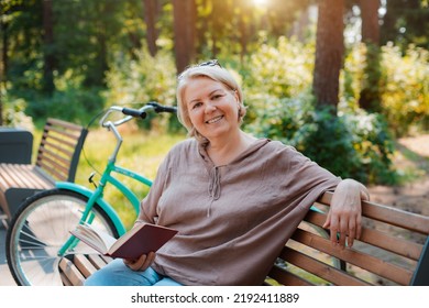 smiling modern old lady relaxing city park. Pensive senior gray haired woman casual sitting bench outdoors reading book. cycling forest park, bicycle, healthy active lifestyle after 50-60 years
