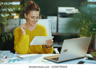 smiling modern small business owner woman in yellow sweater with tablet PC and laptop in the modern green office. - Powered by Shutterstock