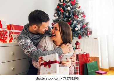 Smiling Modern Young Couple Opening Christmas Gifts