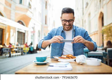 Smiling modern young man taking photo of his meal at the restaurant - Powered by Shutterstock