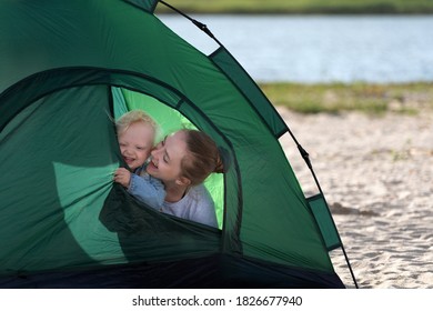 Smiling Mom And Baby Peeking Out Of Tourist Tent. Tent On The Sandy Beach. Camping.