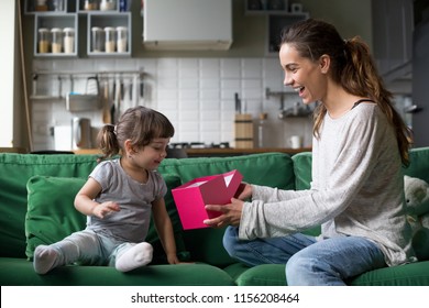 Smiling Mom Giving Excited Daughter Present On Her Birthday, Happy Single Mother And Curious Child Girl Opening Pink Gift Box Together, Cute Kid Receiving Holiday Gift From Mommy Concept