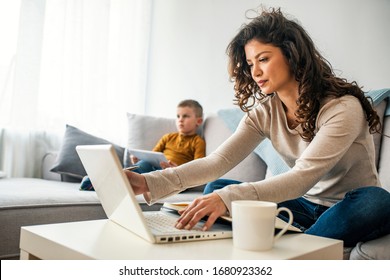 Smiling mom working at home with her child on the sofa while writing an email. Young woman working from home, while in quarantine isolation during the Covid-19 health crisis
