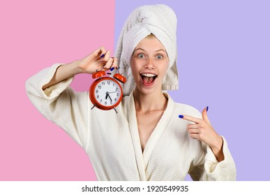 Smiling morning woman with alarm clock. Happy girl in bathrobe with alarm watch. Woman pointing on alarm-clock. Time concept.