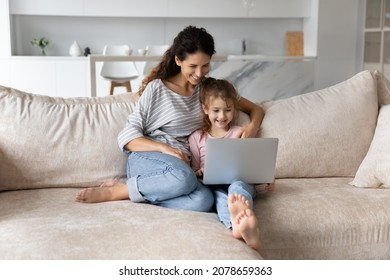 Smiling Mother With Adorable Daughter Using Laptop Sitting On Couch Together, Happy Family Young Mom And Cute Girl Kid Looking At Computer Screen, Chatting Online By Video Call, Watching Cartoons