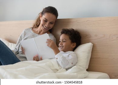 Smiling Mother With African American Child Reading Book, Loving Mom With Little Son Lying In Bed, Caring Mum Reading Fairy Tale, Telling Story To Cute Preschool Boy, Happy Family Relaxing Together