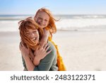 Smiling mother and beautiful daughter having fun at the beach. Portrait of happy woman giving a piggyback ride to cute little girl with copy space. Portrait of happy red hair kid embracing her mom.