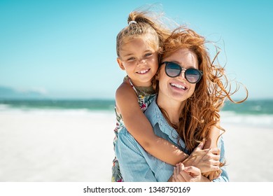 Smiling mother and beautiful daughter having fun on the beach. Portrait of happy woman giving a piggyback ride to cute little girl with copy space. Portrait of kid embracing her mom during summer.
