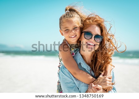 Smiling mother and beautiful daughter having fun on the beach. Portrait of happy woman giving a piggyback ride to cute little girl with copy space. Portrait of kid embracing her mom during summer.