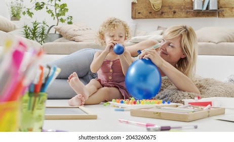 smiling mother with blonde curly haired daughter child, preschool learning activity at home, concept of healthy growing, cheerfully draws and writes playing with inflatable balloons in living room
