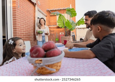 Smiling mother brings food to the table as her family prepares to enjoy a meal together on their sunny balcony. - Powered by Shutterstock