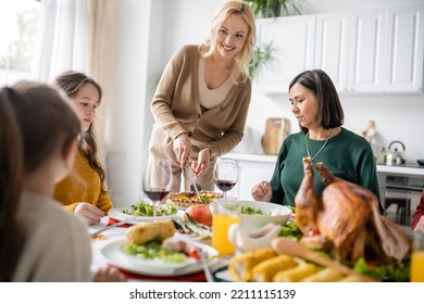 Smiling Mother Cutting Pie Near Multicultural Family And Blurred Thanksgiving Turkey At Home