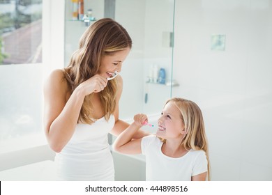 Smiling mother and daughter brushing teeth at home