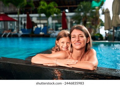 Smiling mother, daughter enjoy poolside embrace at tropical resort. Child, woman hug, laugh in sunny weather by blue water. Family relax, share love summer holiday. Carefree moments, warm bond pool. - Powered by Shutterstock