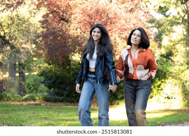 Smiling mother and daughter hold hands while walking in a colorful autumn park, sharing a happy moment. - Powered by Shutterstock