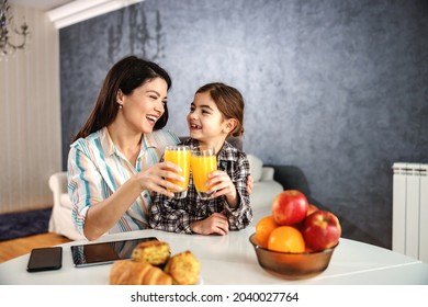 Smiling mother and daughter sitting at dining table and having healthy breakfast. They are toasting with orange juice. - Powered by Shutterstock