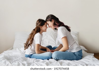 Smiling Mother And Daughter In White T-shirts Sitting On Bed And Touching Foreheads.