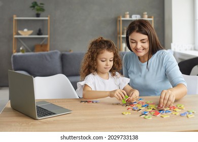 Smiling Mother Or Family Tutor Helping Small Child Learn Foreign Language. Happy Woman And Little Girl Sitting At Desk With Laptop And Developing English Reading Skills Through Fun Engaging Activities