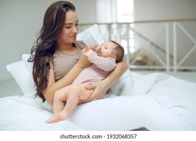 Smiling mother feeding baby boy with fresh milk in plastic bottle in bed closeup. Looking at camera. Motherhood. Childhood. High quality photo.