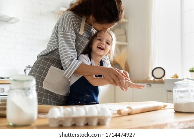 Smiling Mother Having Fun With Small Preschool Kid Daughter, Playing With Dough In Kitchen. Happy Adorable Little Child Girl In Apron Enjoying Cooking Homemade Pastry Together With Mommy At Home.