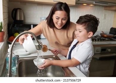 Smiling mother helping son to rinse dishes under tap water after cleaning - Powered by Shutterstock