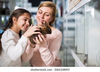 Smiling Mother With Her Happy Daughter Holding Cute Rabbit Together At Pet Store