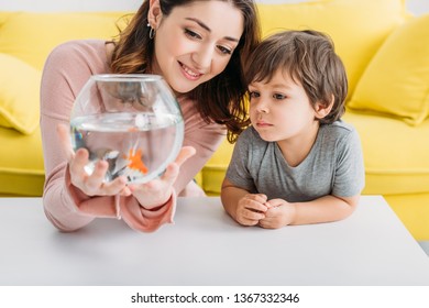 Smiling Mother Holding Fish Bowl Near Adorable Son At Home