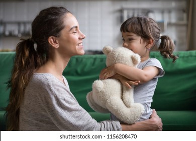 Smiling Mother Hugging Cute Little Girl Holding Teddy Bear Toy Showing Love And Care In Family, Young Mom Embracing Protecting Child, Sincere Relationships Between Mum And Daughter Cuddling Concept