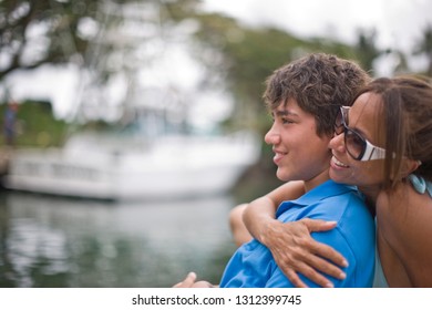 Smiling Mother Hugging Her Teenage Son From Behind.