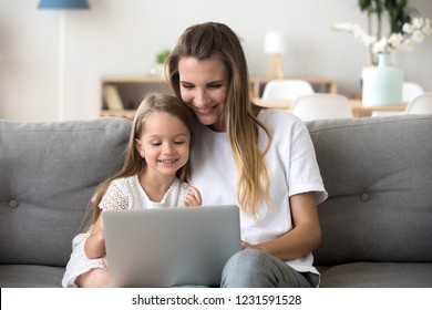 Smiling Mother And Kid Daughter Having Fun Shopping Online Sitting On Sofa, Happy Mom Baby Sitter Teaching Little Child Girl Use Laptop Application, Watching Cartoon Or Making Video Call On Computer