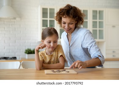 Smiling Mother And Little Daughter Playing Logic Strategy Wooden Board Game At Kitchen Table Together, Caring Mom Teaching Adorable Kid Girl, Happy Family Engaged In Educational Activity At Home