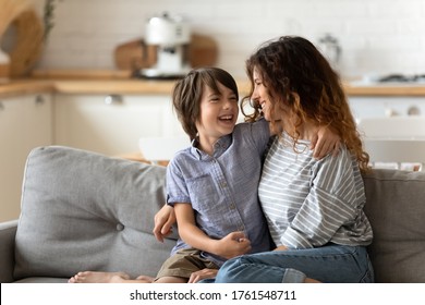 Smiling Mother And Little Son Hugging Looking At Each Other. Loving Mum And Cute Child Boy Laughing Sitting On Couch Enjoying Tender Moment At Home. Having Fun Together Good Family Relationship.