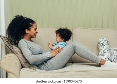 Smiling Mother Lying On Couch With Her Baby On Hips