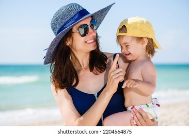 Smiling mother put sun screen protection cream on toddler baby face, family fun during happy vacation at sea beach - Powered by Shutterstock