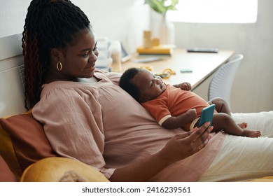 Smiling mother resting on bed with little baby and texting friends - Powered by Shutterstock