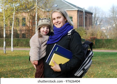 smiling mother with school equipment carries her daughter