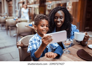 Smiling mother sitting in public cafe with son taking selfie - Powered by Shutterstock