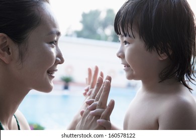 Smiling mother and son face to face and holding hands by pool