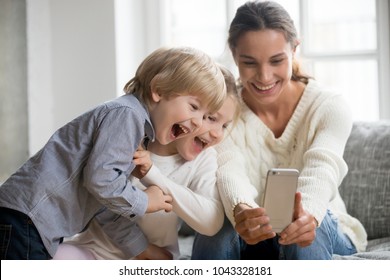 Smiling Mother Taking Selfie With Cute Kids On Smartphone, Happy Young Mom Laughing Making Photo With Little Son And Daughter At Home, Single Mommy And Adopted Children Playing Having Fun With Phone