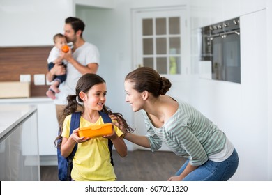 Smiling Mother Talking To Daughter Holding Lunch Box At Home