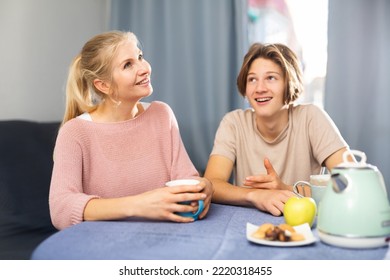 Smiling Mother With Teenage Son Drinking Tea And Talking At Table At Home Indoors