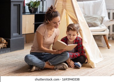 Smiling mother tell fairytale to son at home. Good family pastime on weekend. Adopted child and baby sitter. Mom read interesting story schoolboy kid. Wigwam in cozy living room. Educational process
