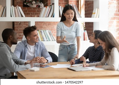 Smiling motivated asian female team leader holding meeting with diverse groupmates, explaining new project detail. African american, indian and caucasian concentrated students discussing assignment. - Powered by Shutterstock