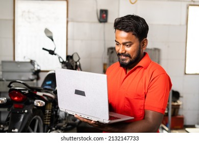 Smiling motorbike mechanic busy using laptop at garage - concept of technology, checking online booking and maintenance and repair service. - Powered by Shutterstock